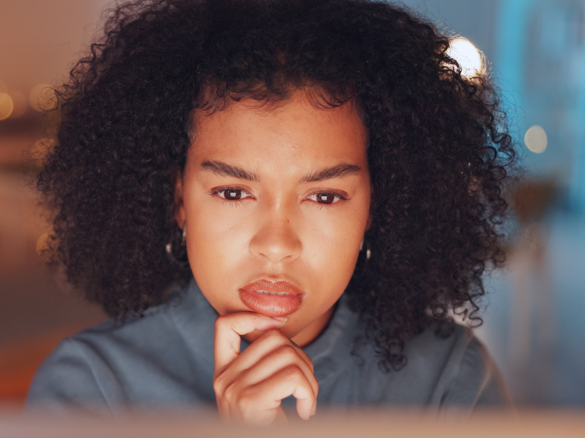 A woman looking thoughtfully at her laptop screen